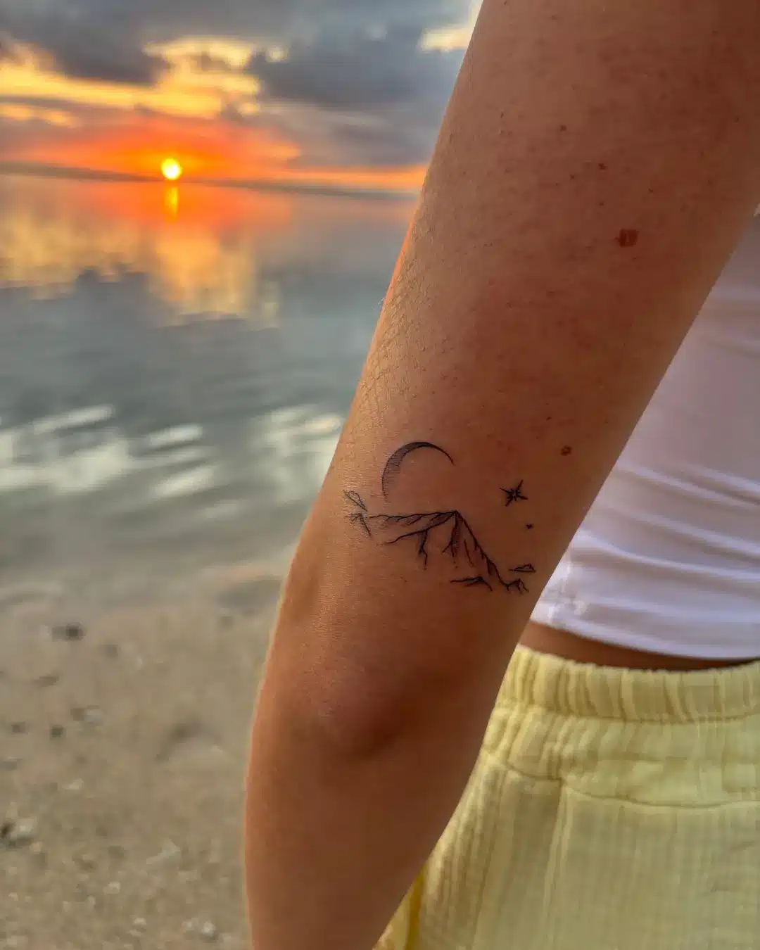 Tatouage fine line montagne, lune et étoiles photographié au coucher du soleil à La Réunion