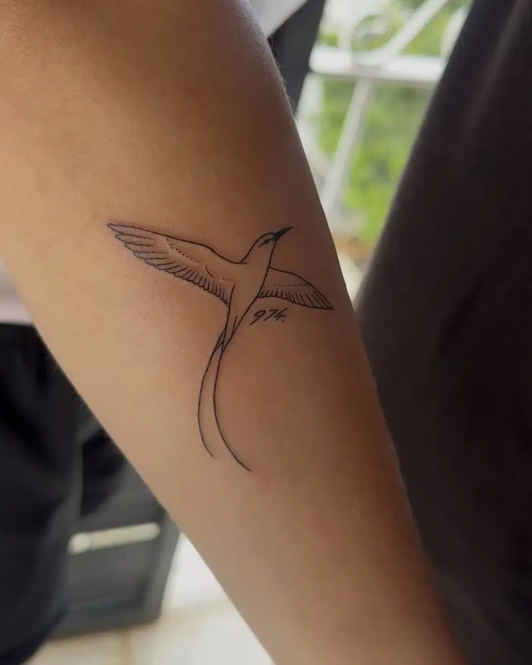 Tatouage fine line d'un paille-en-queue en vol avec l'inscription 974